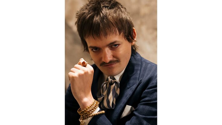 Jack Gleeson as the character Wentworth wearing gold jewellery and looking down to camera